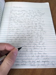 A page of handwritten words in a lined notebook and hand holding mechanical pencil
